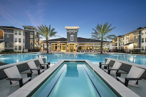A swimming pool surrounded by lounge chairs in front of a building.