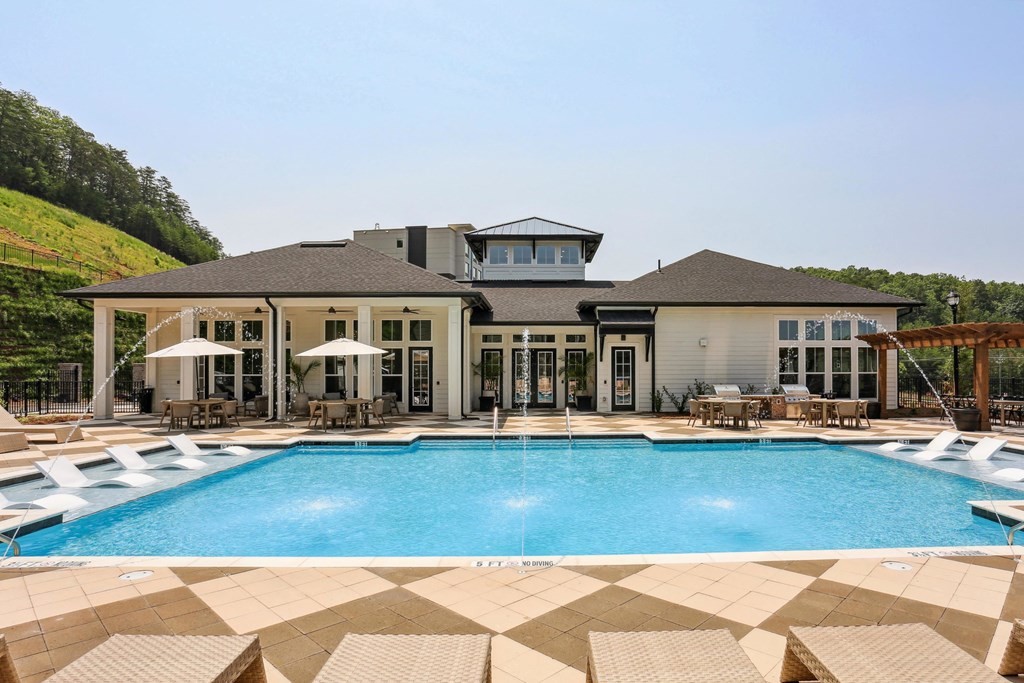 a pool with lounge chairs and umbrellas in front of a house