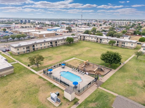 A large grassy area with a pool and apartment buildings in the background.