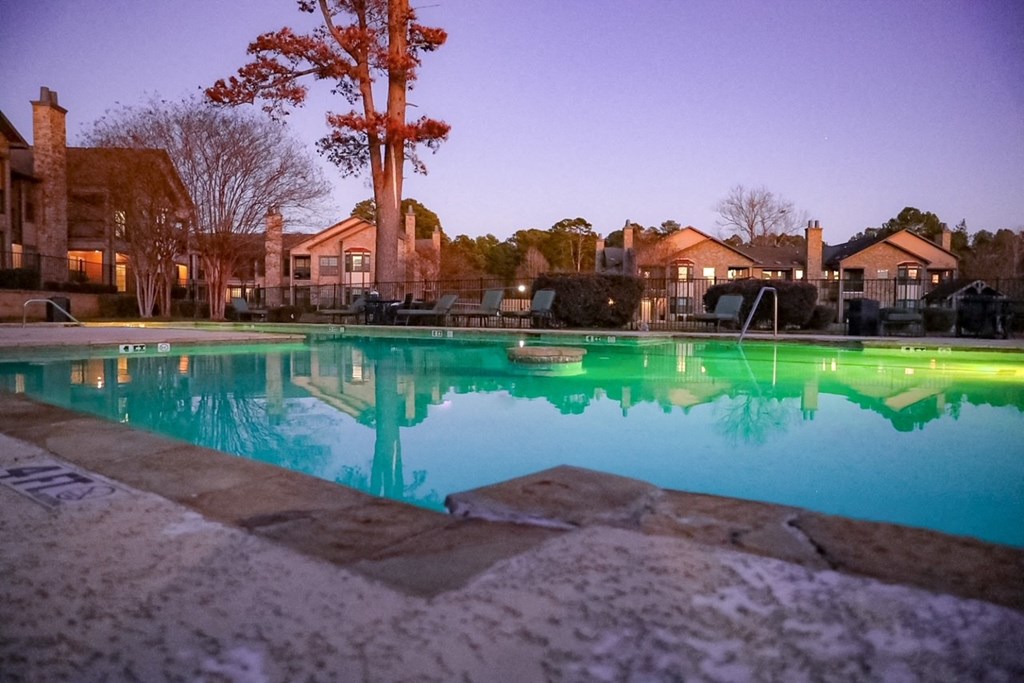 a swimming pool at night with houses in the background