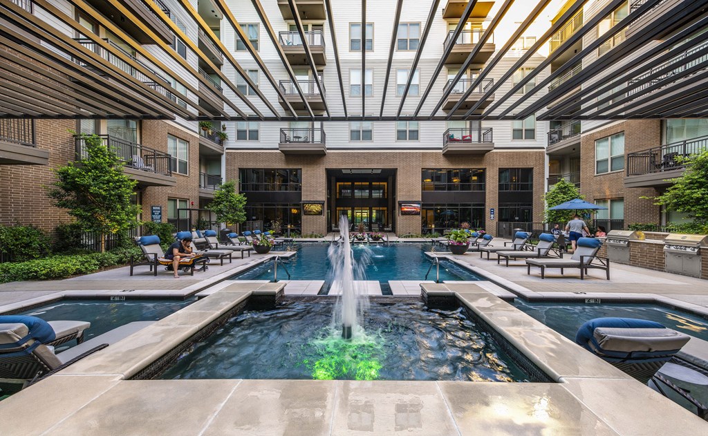 a pool with a fountain and lounge chairs in front of an apartment building