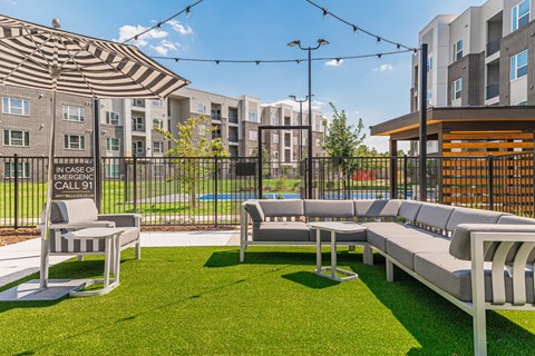 a lounge area with couches and chairs on a lawn with an apartment building in the background