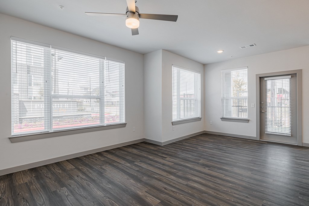 an empty living room with a ceiling fan and three windows