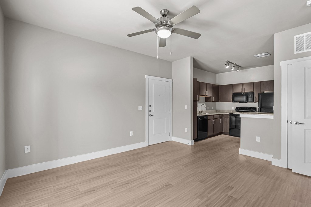 an empty living room with a ceiling fan and a kitchen