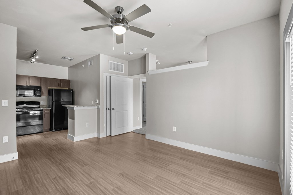 an empty living room with a ceiling fan and a kitchen