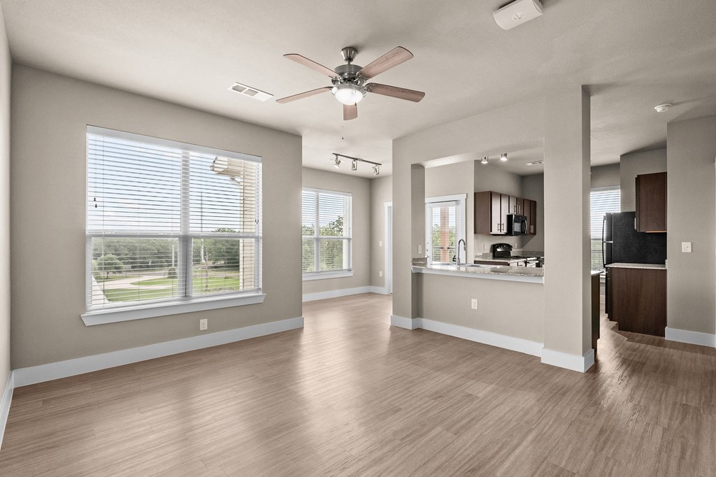 an empty living room with a ceiling fan and a kitchen