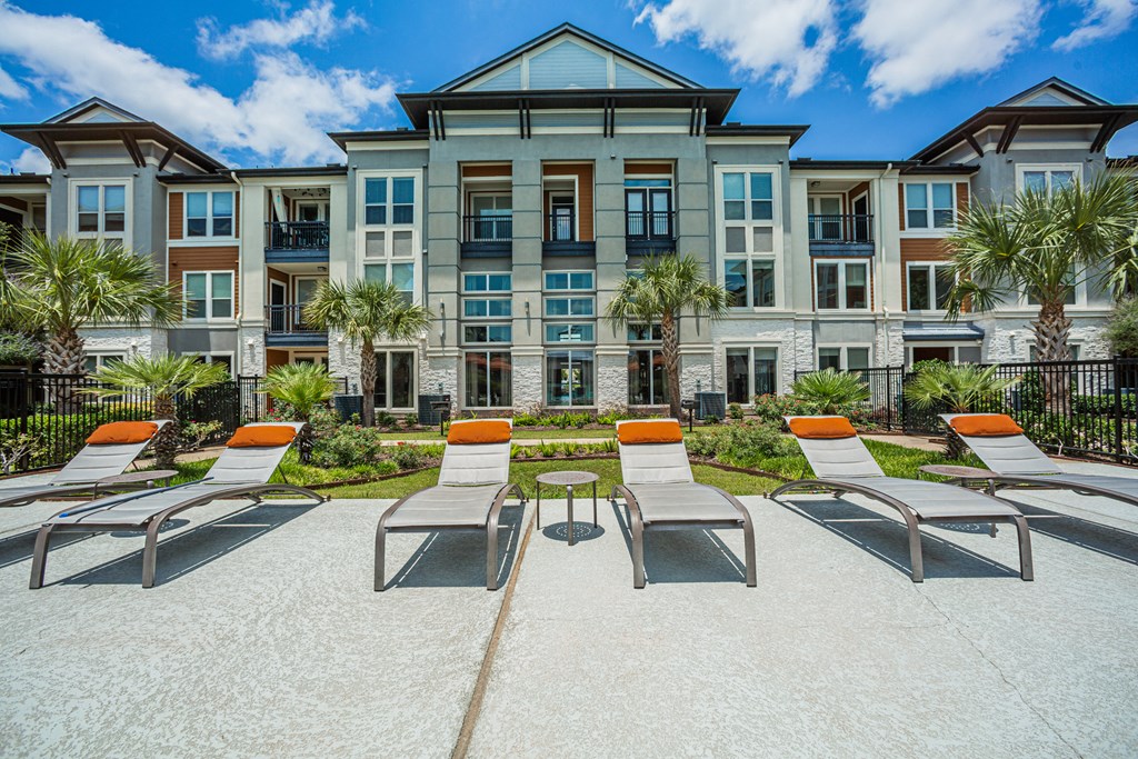 a patio with lounge chairs and tables in front of an apartment building