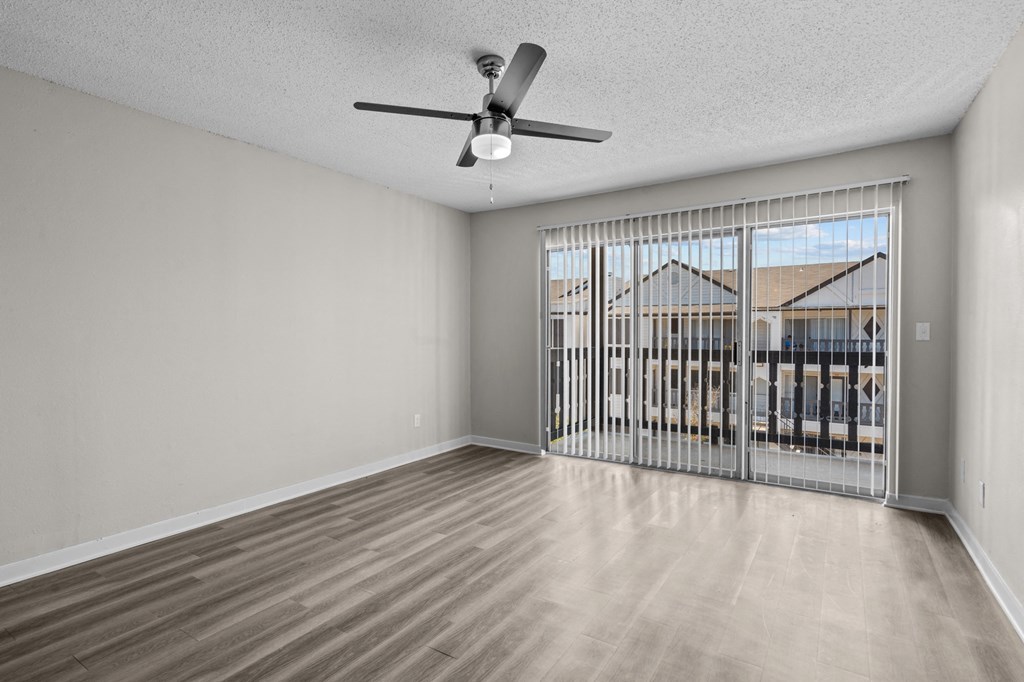 an empty living room with a large window and a ceiling fan