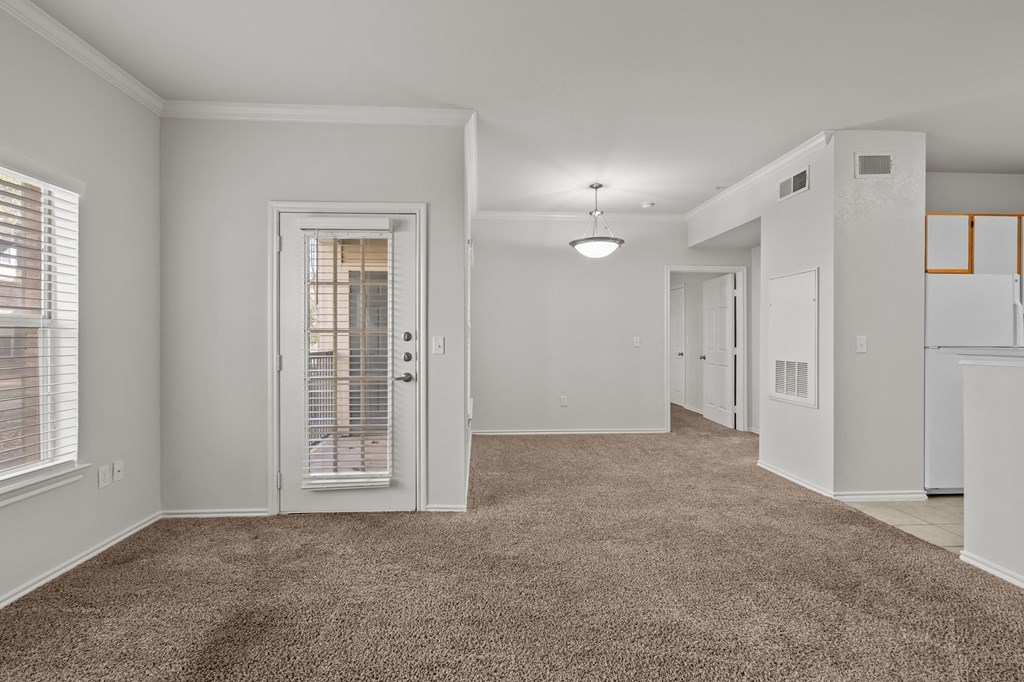 a spacious living room with a door to the kitchen and a carpeted floor