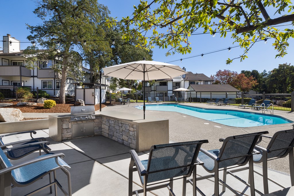 A pool surrounded by chairs and umbrellas with a house in the background.