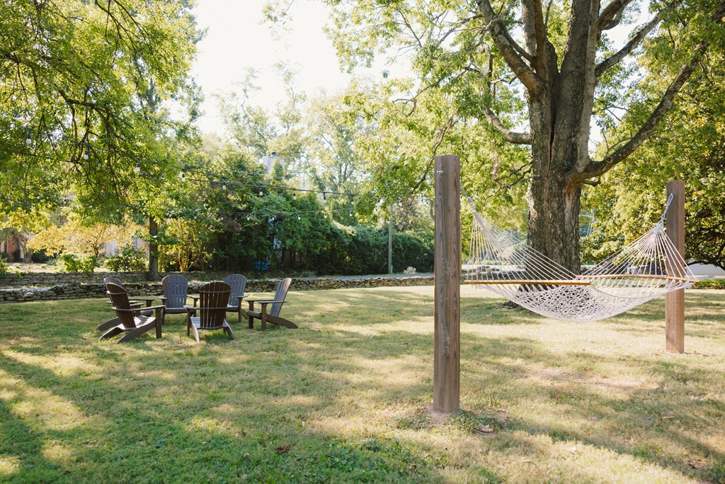 A hammock is strung between two wooden posts in a grassy area with chairs and a table nearby.