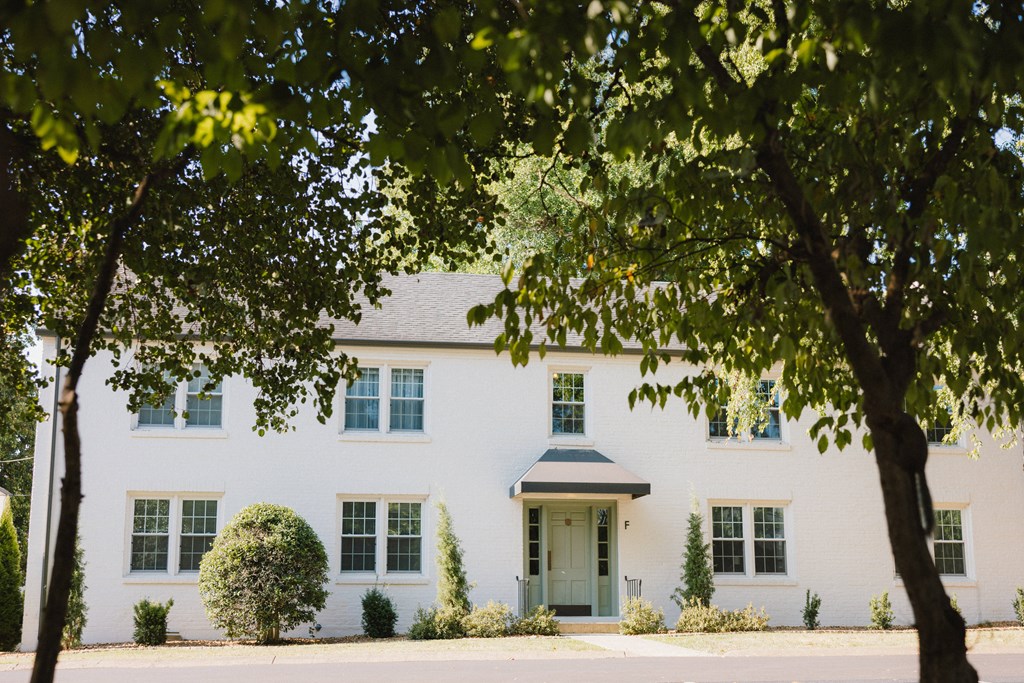 A white house with a grey roof and a green door is surrounded by trees.