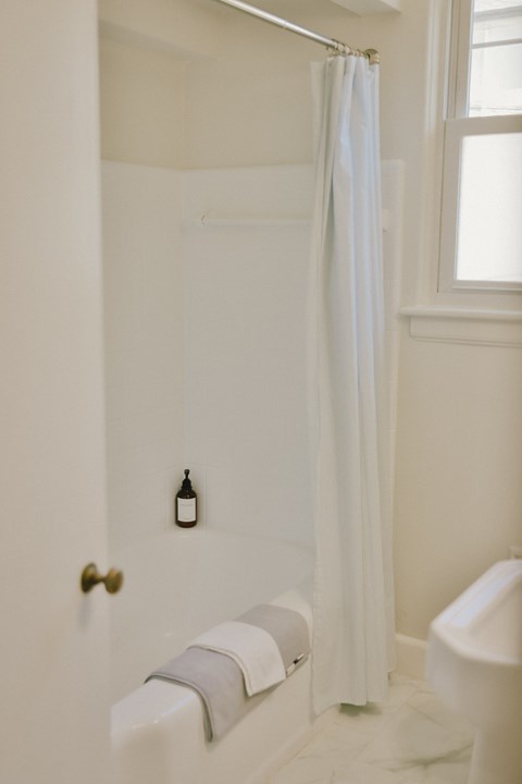 A white bathroom with a toilet, a shower with a white curtain, and a bottle on the wall.