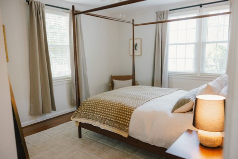 A bedroom with a four poster bed and a table with a lamp on it.