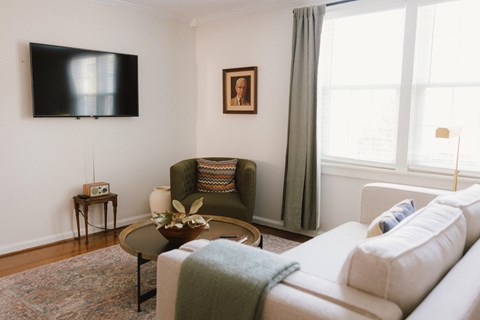 A living room with a white couch, a green chair, and a flat screen TV mounted on the wall.