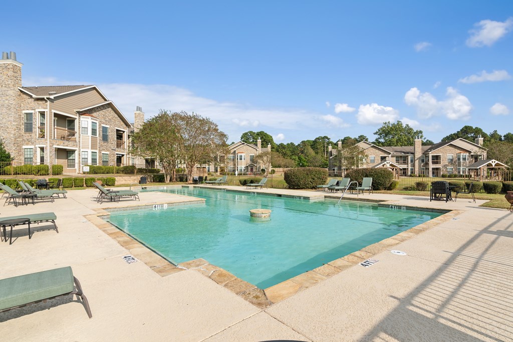 A large swimming pool surrounded by a concrete patio and lounge chairs.