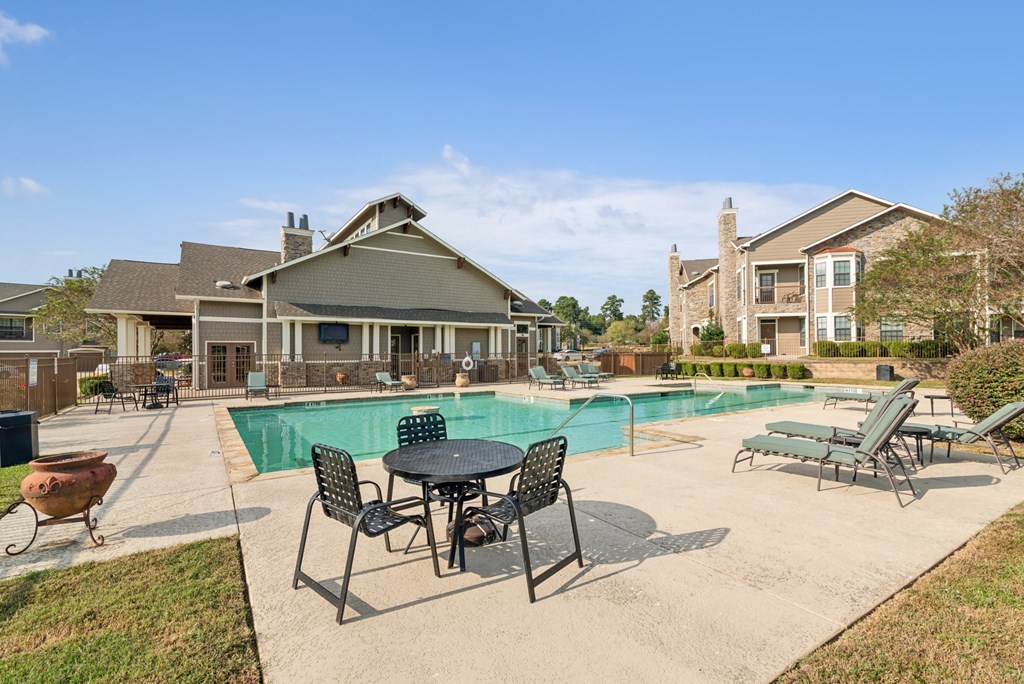A pool area with a table and chairs in front of a building.