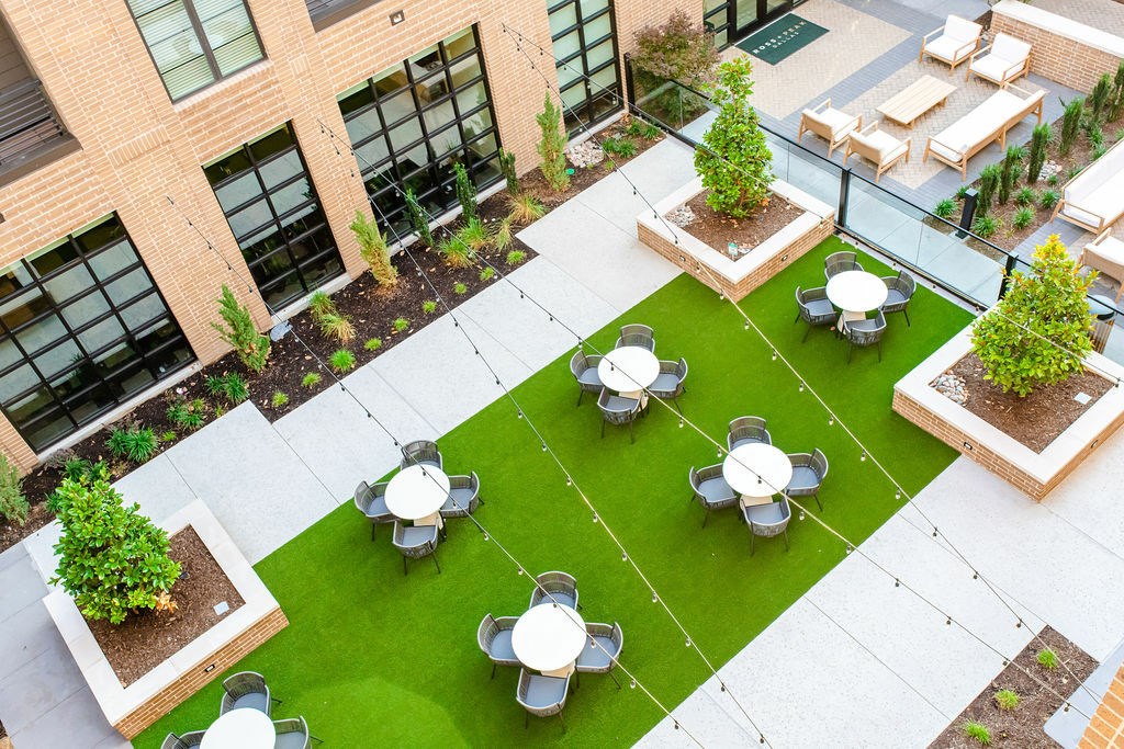 A courtyard with a green lawn and white tables.