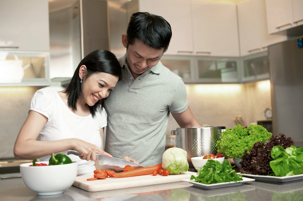 A man and woman are preparing a salad in a modern kitchen.