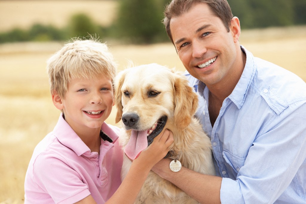 A man and a boy are hugging a dog in a field.