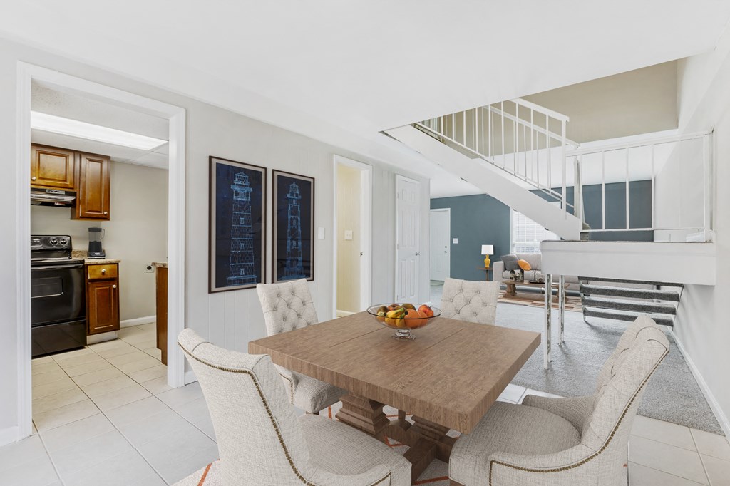 a dining area with a wooden table and chairs and a kitchen with a staircase