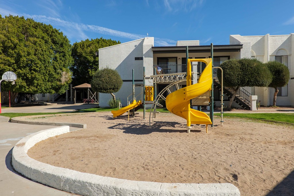 A playground with a yellow slide and a basketball court.