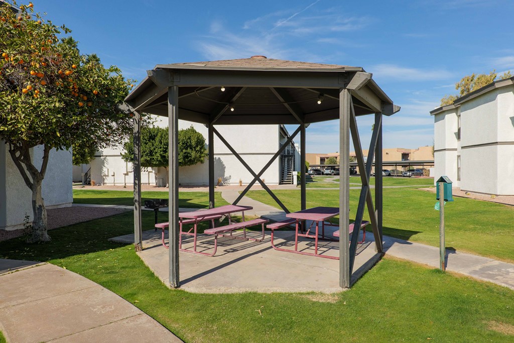 A picnic shelter with a table and benches is situated in a grassy area.