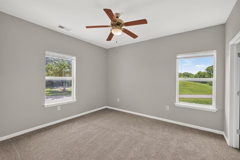A room with a ceiling fan and two windows.