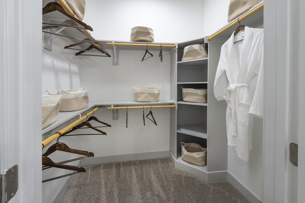 a walk in closet with a white wall and shelves filled with shoes and hangers