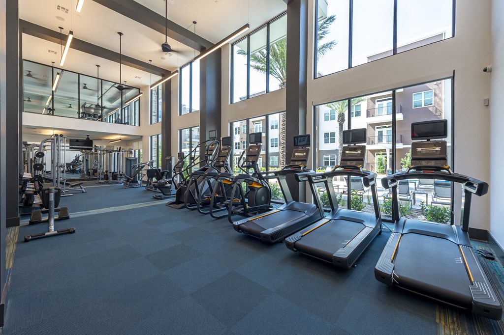 a gym with cardio equipment and windows in the lobby of a building