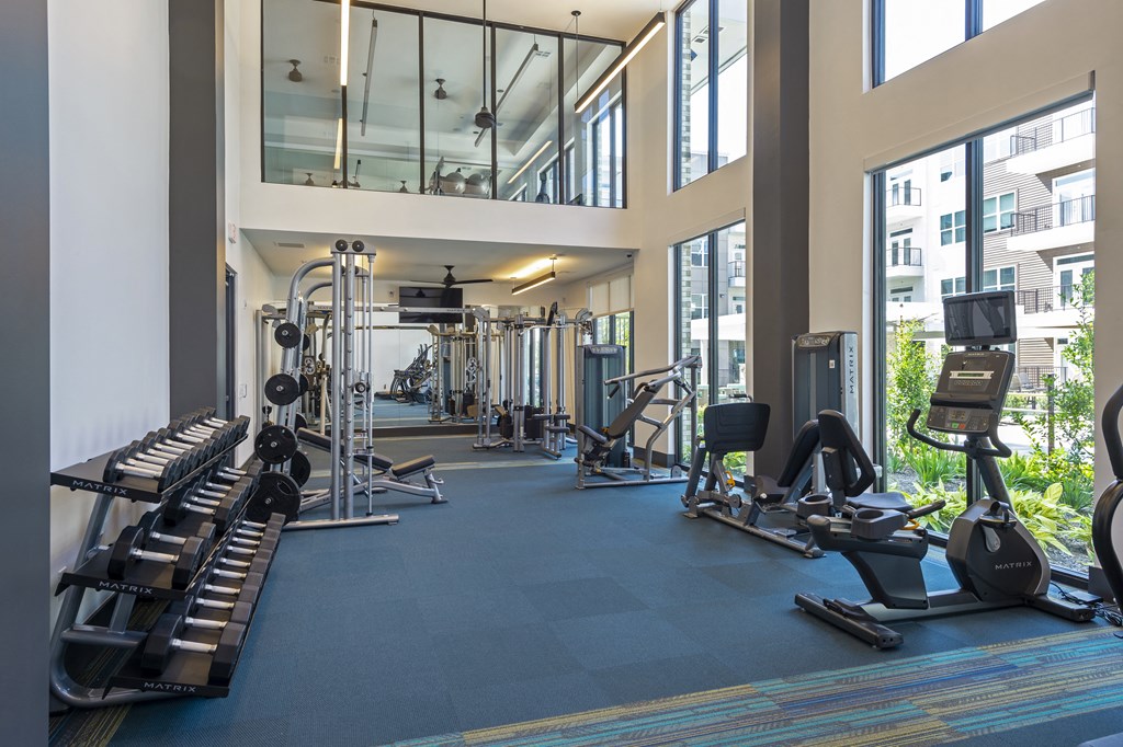 a gym with cardio machines and weights in a building with large windows