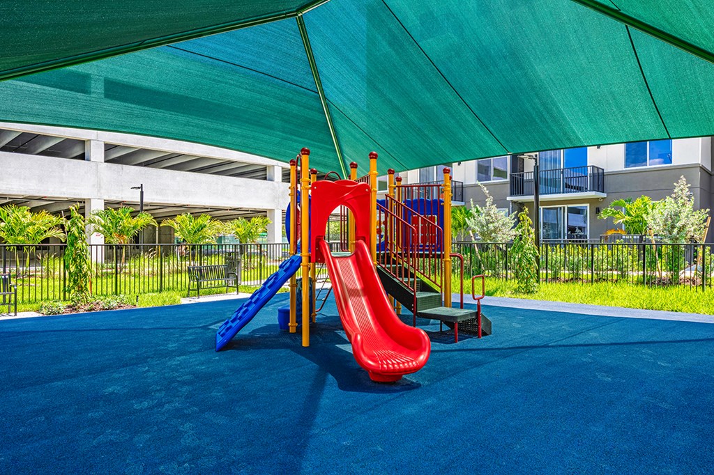 A playground with a red slide and a blue slide under a green canopy.