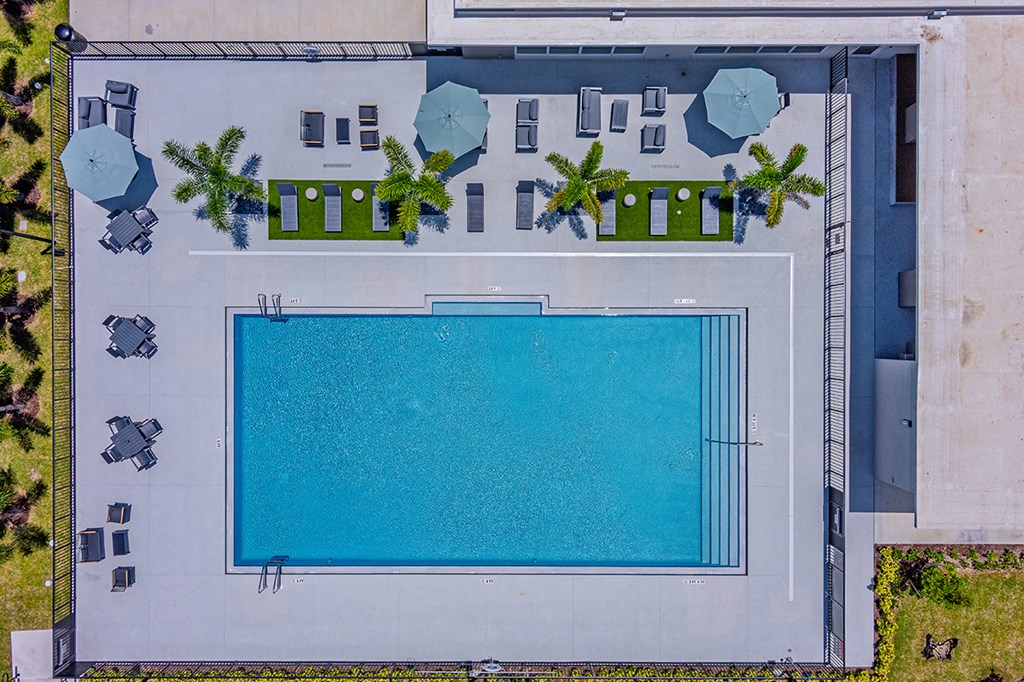 An aerial view of a swimming pool surrounded by a concrete patio and a concrete building.