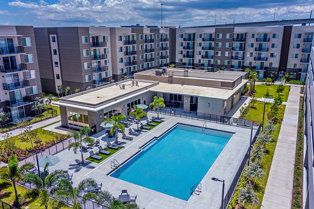 A large swimming pool is surrounded by a concrete patio and lounge chairs.