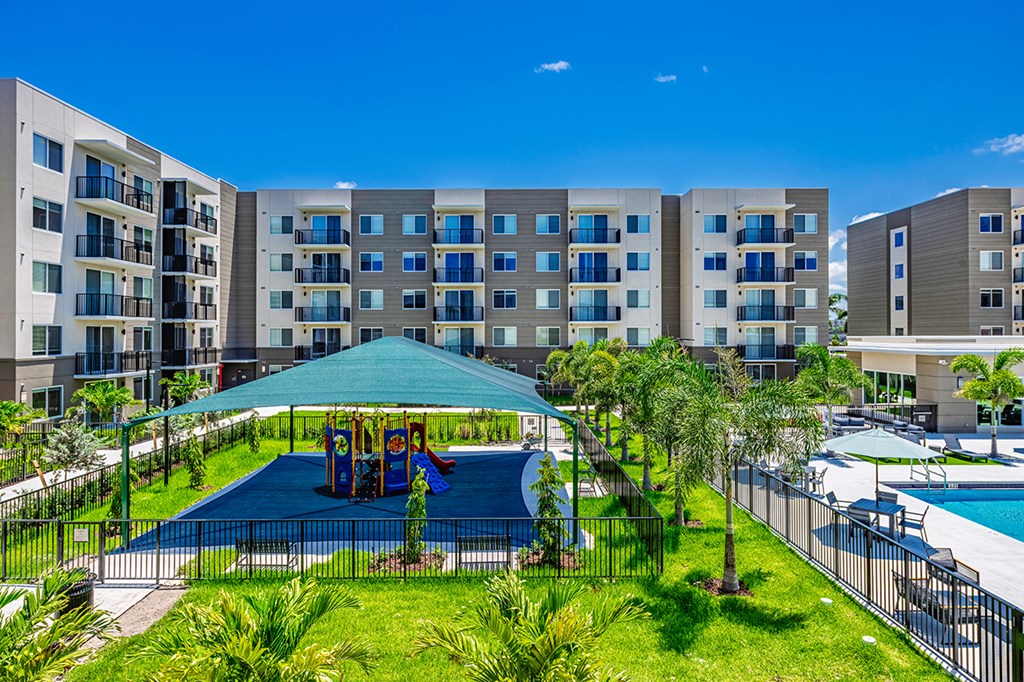 A playground area with a slide and swings is surrounded by a fence and a pool is visible in the background.