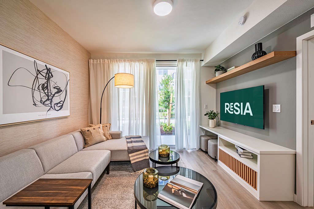 A living room with a grey sofa, a coffee table, a flat screen TV, and a painting on the wall.