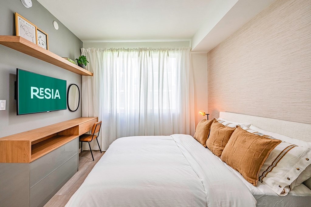 A bedroom with a bed, a desk, and a shelf with a sign that says "RESIA".
