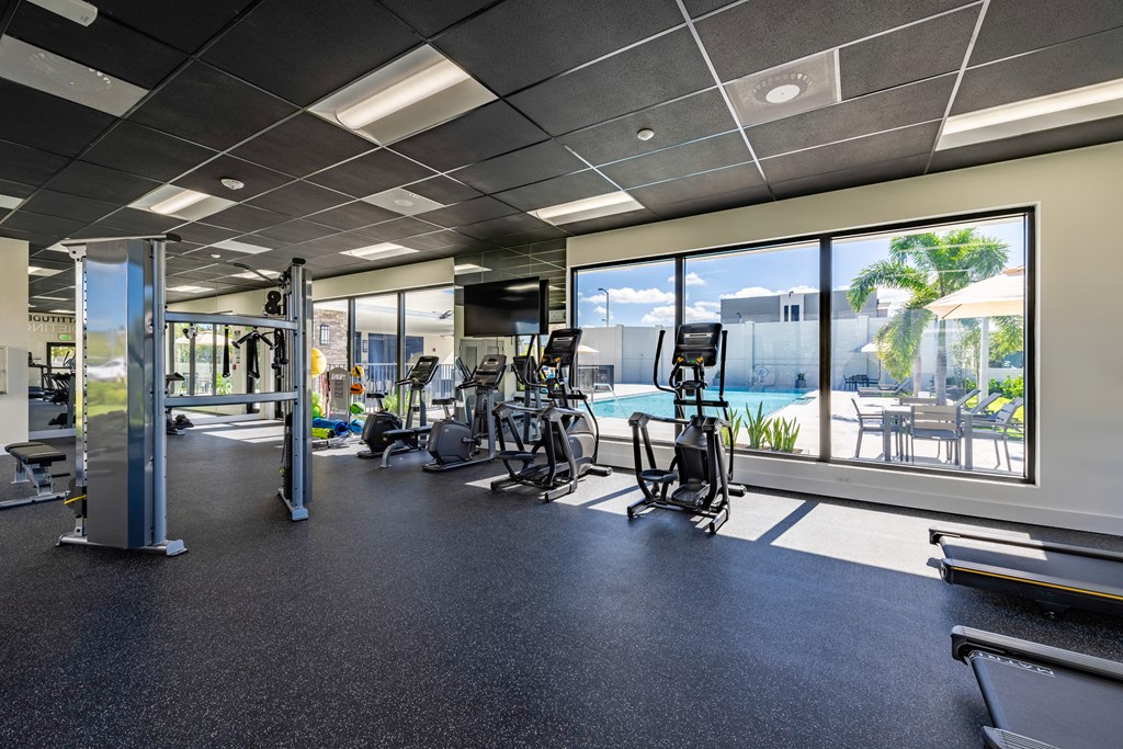 a gym with cardio equipment and windows overlooking a swimming pool the gym  at a residential apartment community Resia in Decatur GA