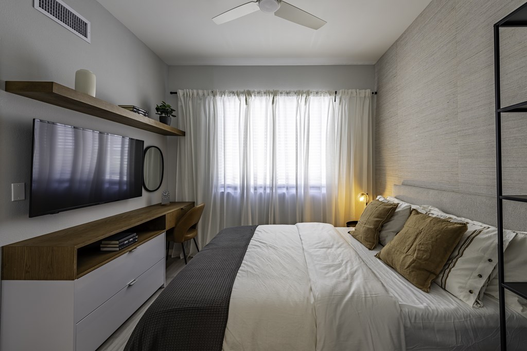 A bedroom with a bed, a television, and a ceiling fan.
