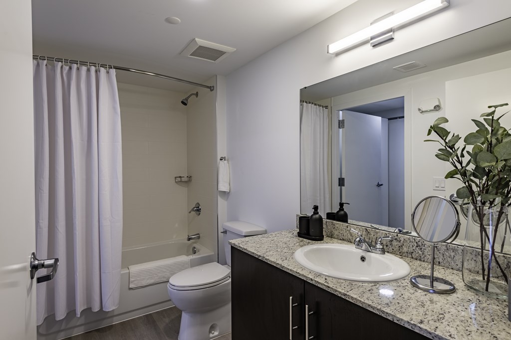 A bathroom with a white toilet, sink, and a shower with a white curtain.