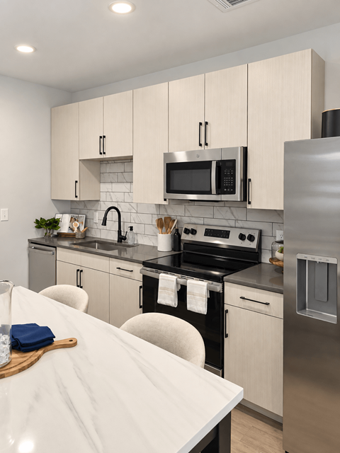 A modern kitchen with a stainless steel refrigerator, microwave, and oven.