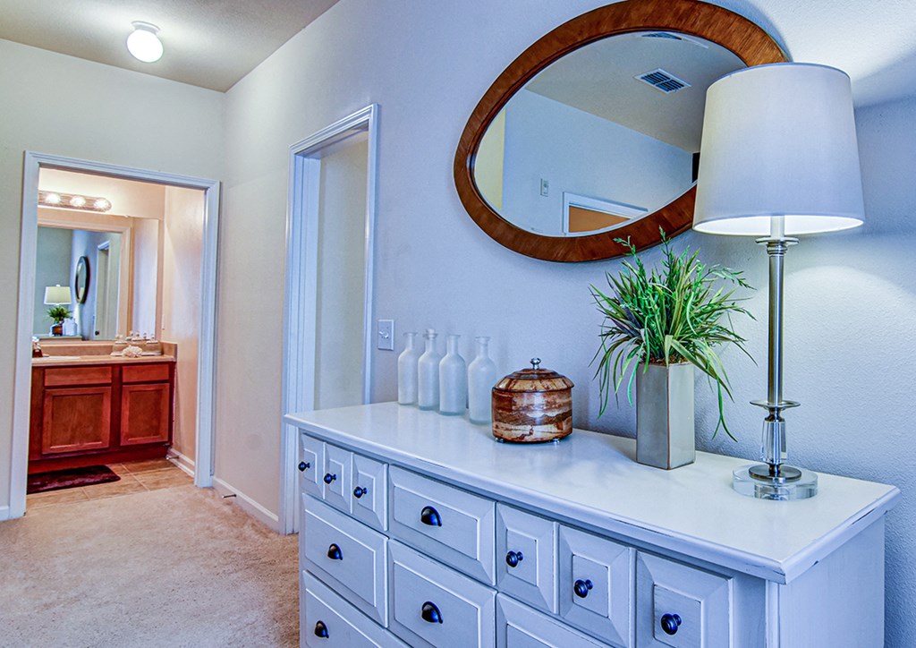 A white dresser with a round mirror above it and a potted plant on top.