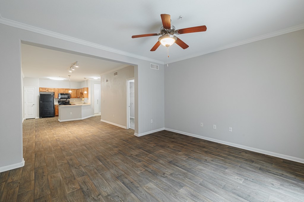 an empty living room with a ceiling fan and a kitchen