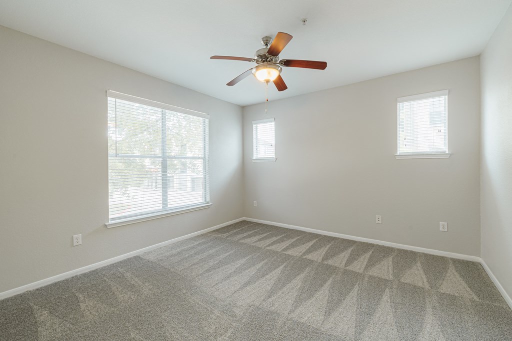 an empty living room with a ceiling fan and two windows