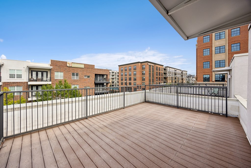 A wooden deck with a metal railing and buildings in the background.