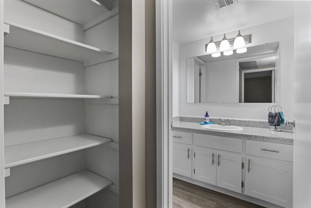A white pantry with an empty fridge and a bathroom with a sink and mirror.