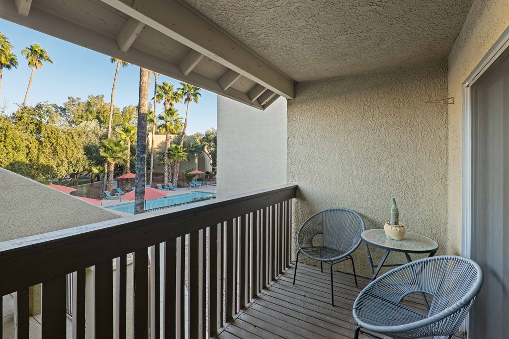A balcony with a table and two chairs overlooking a pool and palm trees.
