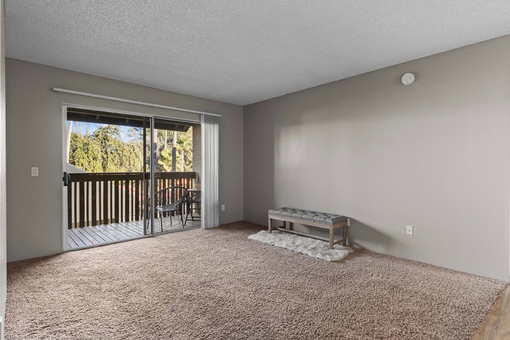 A room with a carpeted floor and a sliding glass door leading to a deck.