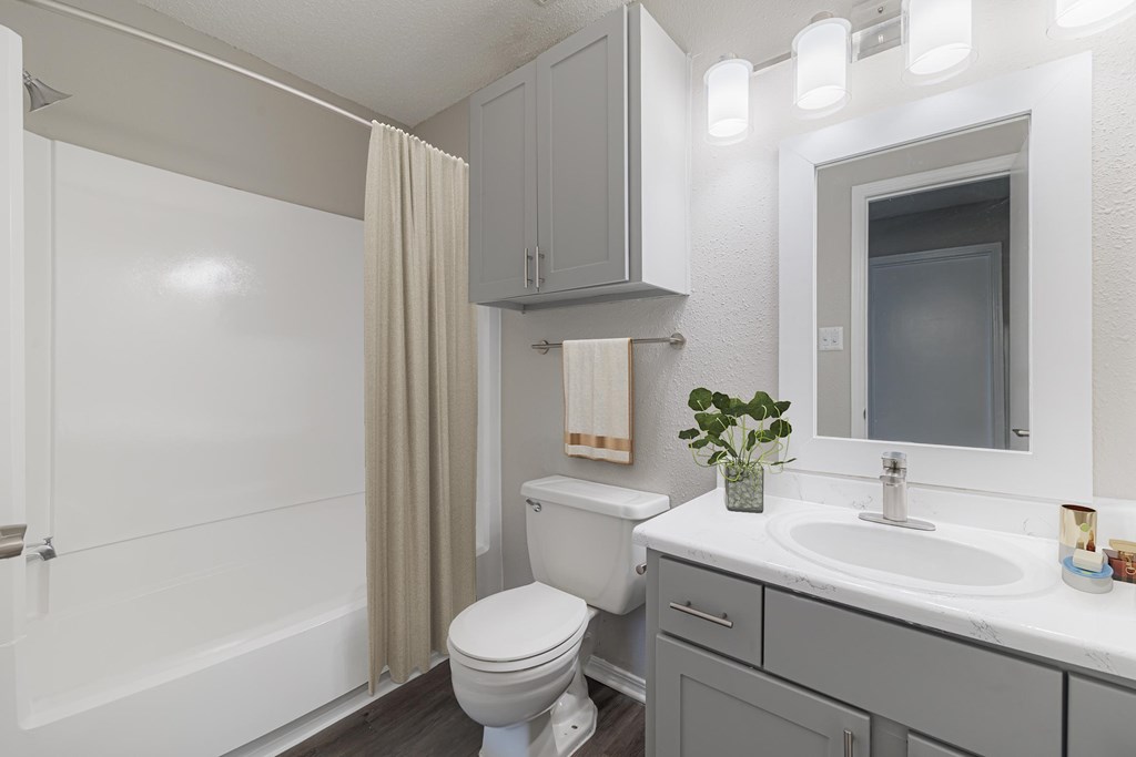 A white toilet sits in a bathroom with a white sink and a white shower.