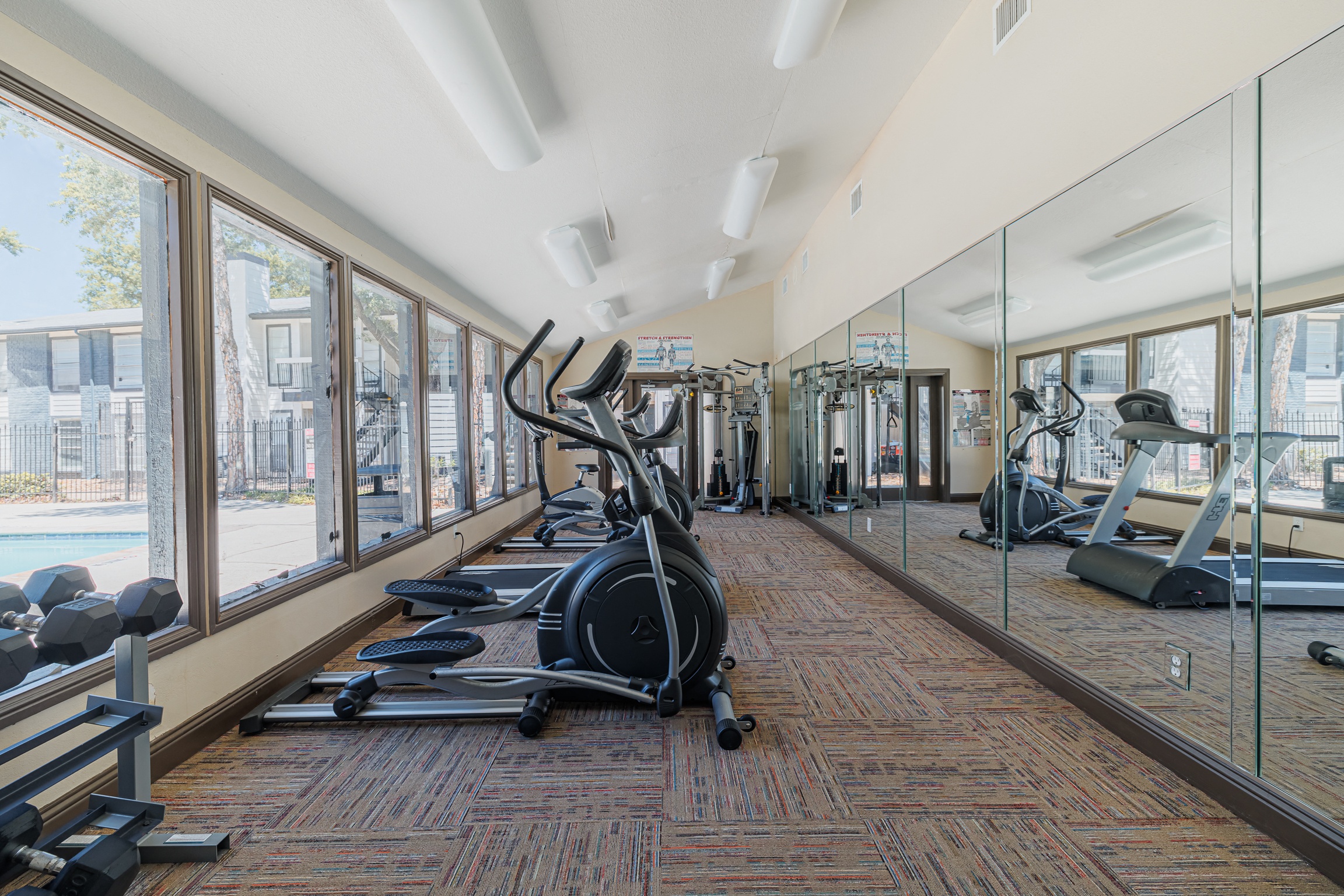 a gym with cardio equipment and windows at the district at highland village apartments